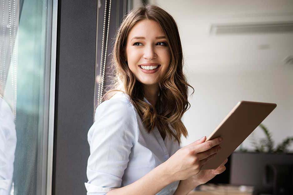 Happy woman manager holding tablet and standing in modern office